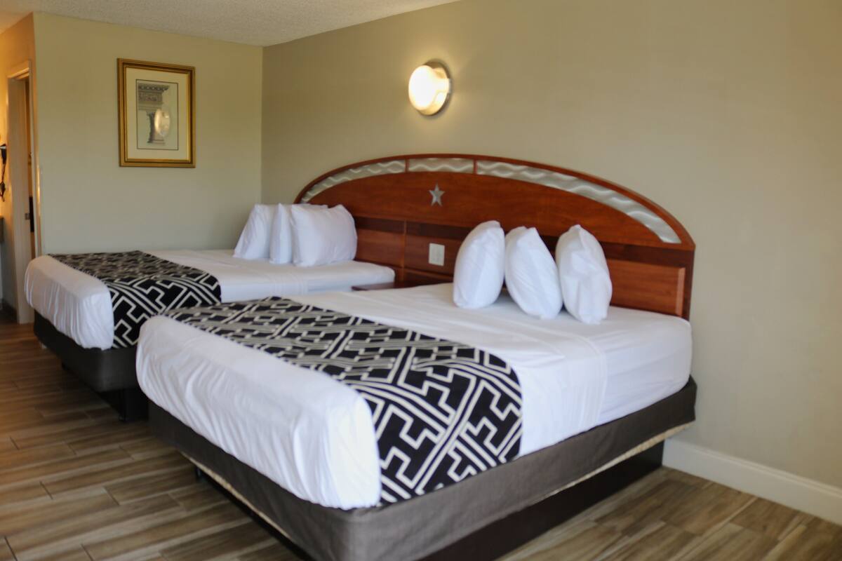 A hotel room with two beds, each with a headboard, white bedding, and a patterned throw blanket.
