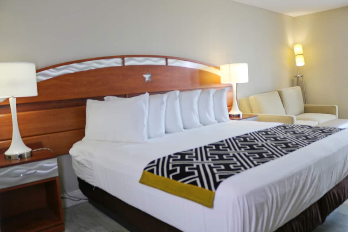 A hotel room with a large bed, two bedside lamps, a chair, and a nightstand.