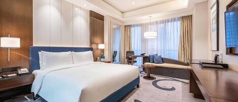 A hotel room with a large bed, a sofa, a desk, and a TV.