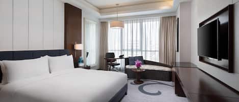 A hotel room with a large bed, a sofa, a TV, and a view of the city.