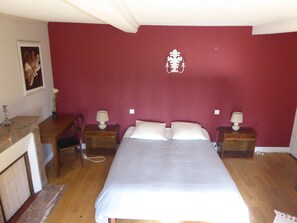 A bedroom with a large bed, two bedside tables with lamps, a wooden nightstand, a chair, and a wall-mounted decorative piece. - La Ferme Des Vignes (Hotot-en-Auge)