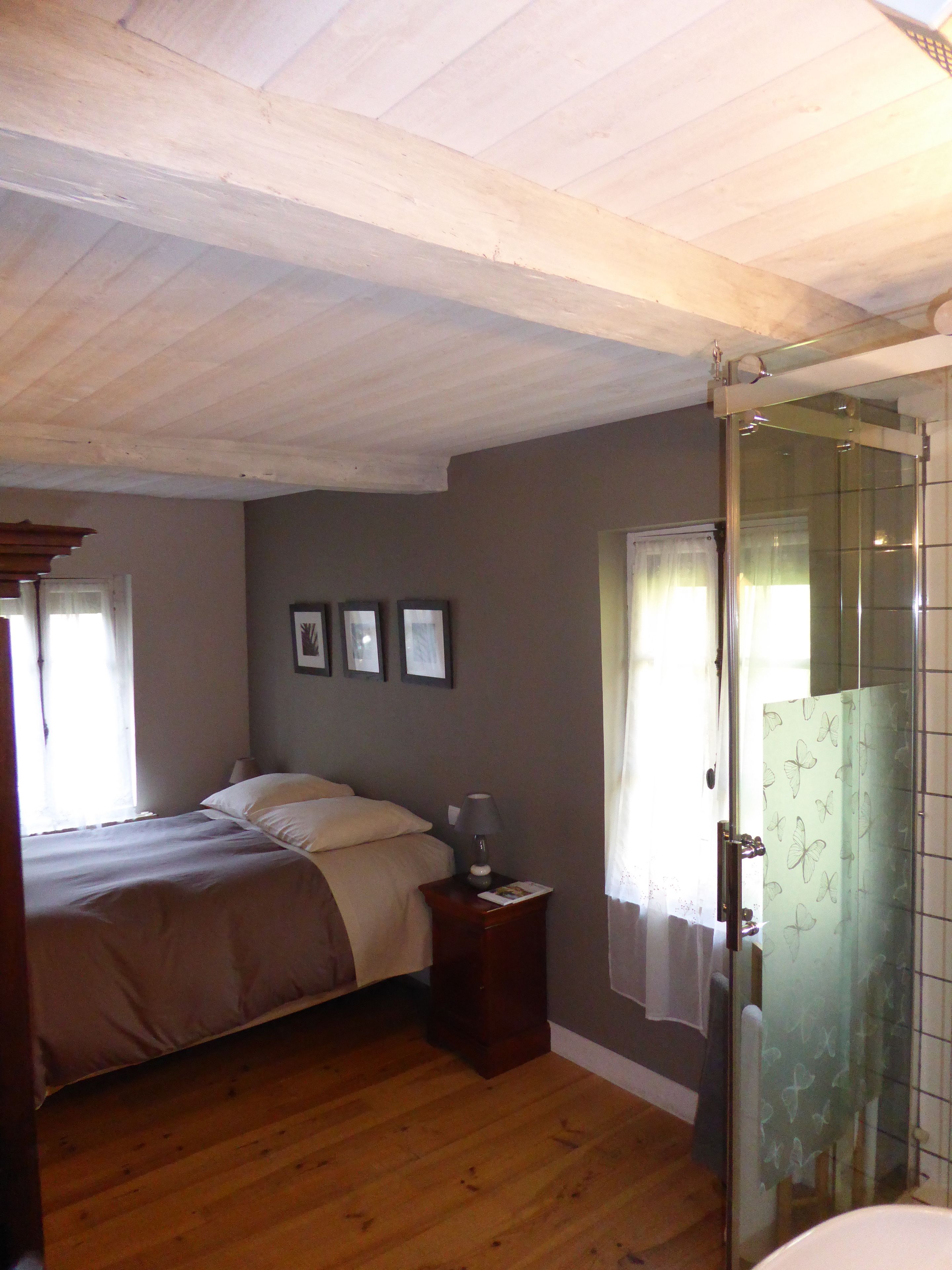 A bedroom with a bed, a nightstand, a framed picture, a window with curtains, and a shower area.