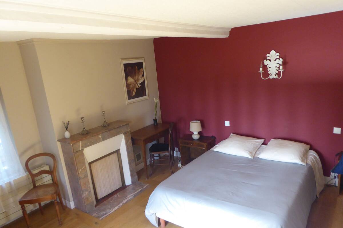 Un dormitorio con una cama, un escritorio, una silla, una chimenea y una lámpara de pared.
