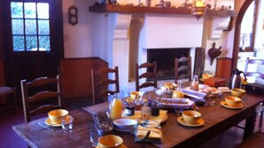 A dining room with a long table set for a meal, chairs around, and a fireplace in the background. - La Ferme Des Vignes (Hotot-en-Auge)