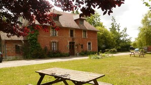 A brick house with a garden and a picnic table in the foreground. - La Ferme Des Vignes (Hotot-en-Auge)