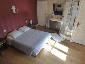 A bedroom with a bed, a nightstand, a dresser, a mirror, and a shower area. - La Ferme Des Vignes (Hotot-en-Auge)