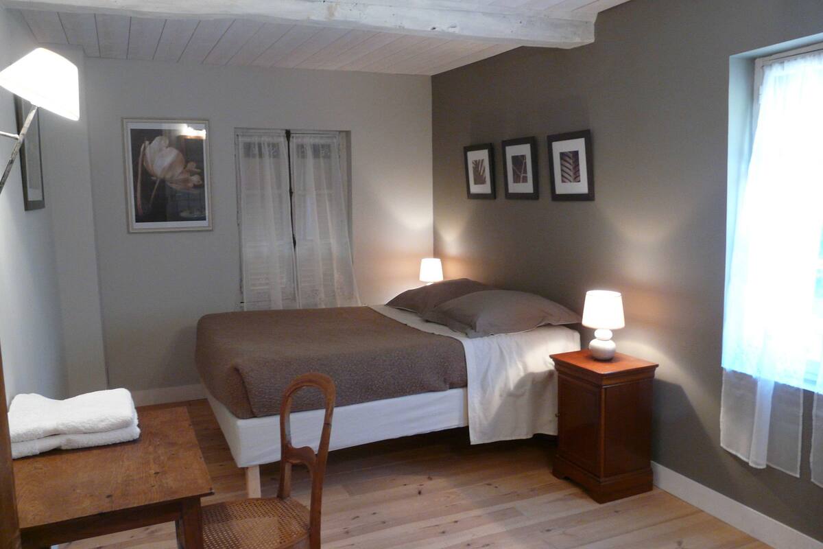 Un dormitorio con una cama, dos lámparas de noche, una silla, una mesa y una ventana con cortinas.