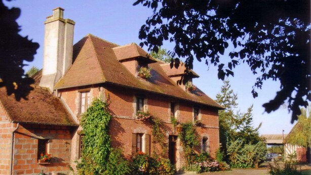 A traditional brick house with a chimney, ivy-covered walls, and a garden with flowers and plants. - La Ferme Des Vignes (Hotot-en-Auge)