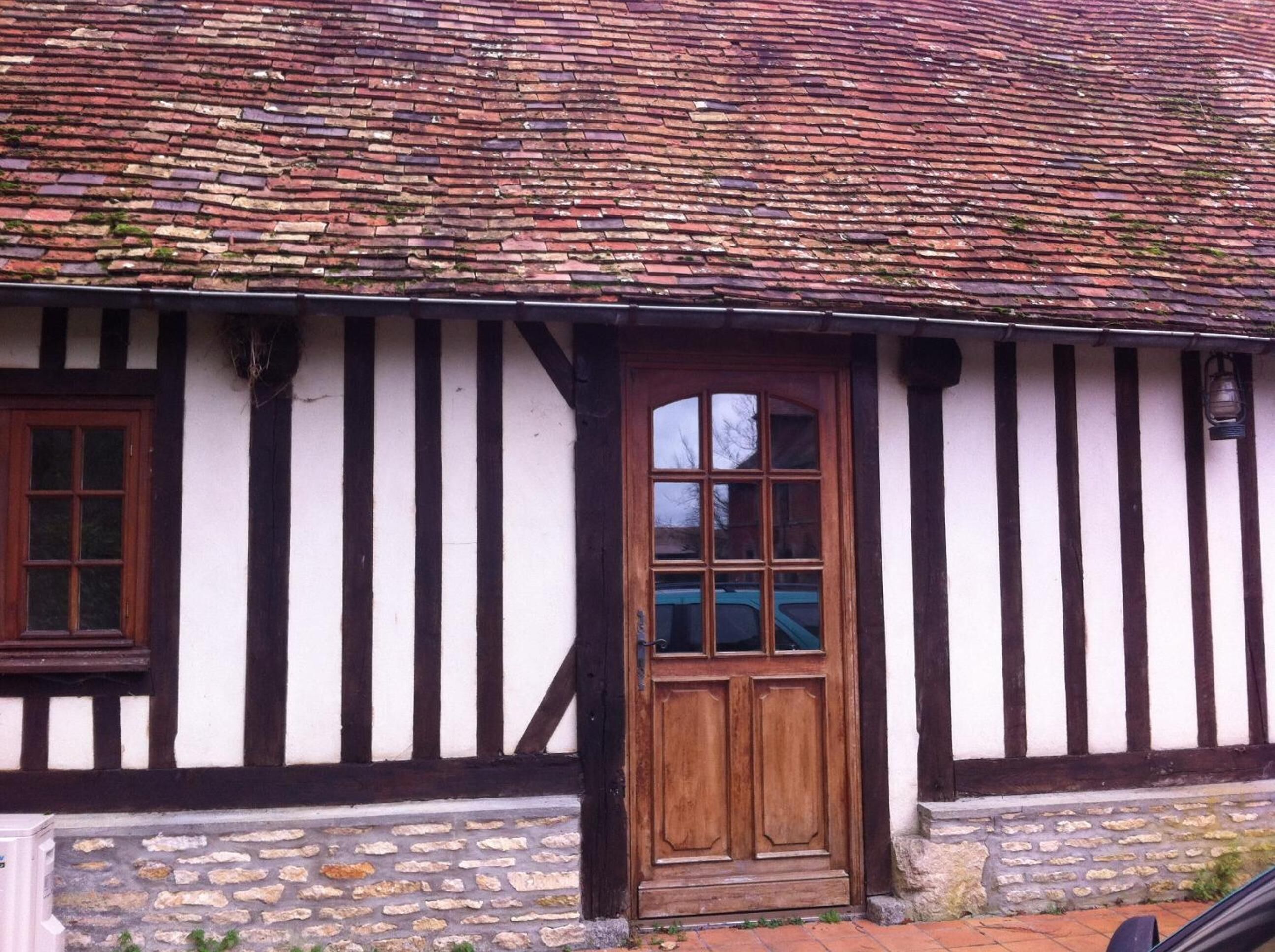 A traditional half-timbered house with a wooden door and windows, stone foundation, and a tiled roof.