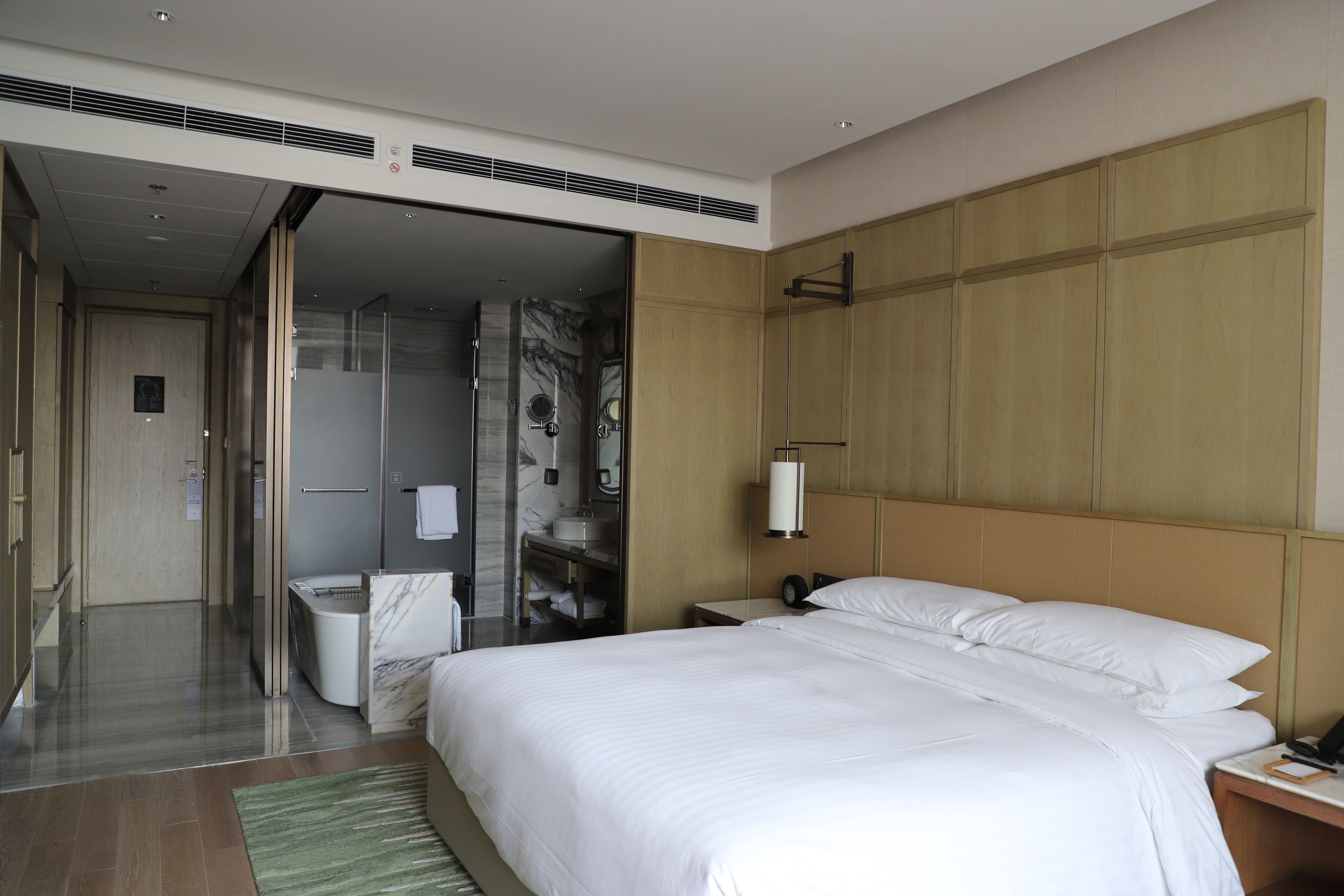 A hotel room with a large bed, a bedside table, a nightstand, a mirror, and a bathroom with a shower and toilet.