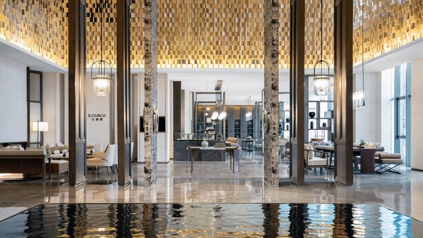 Un vestíbulo amplio con suelo reflectante, mobiliario moderno y techo de madera decorativo.