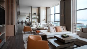Una sala de estar moderna con un sofá, una mesa de centro y sillas. Se observa un televisor y una estantería al fondo.