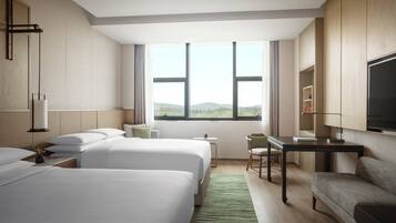 A hotel room with two beds, a desk, a chair, a TV, and a view of the outdoors.