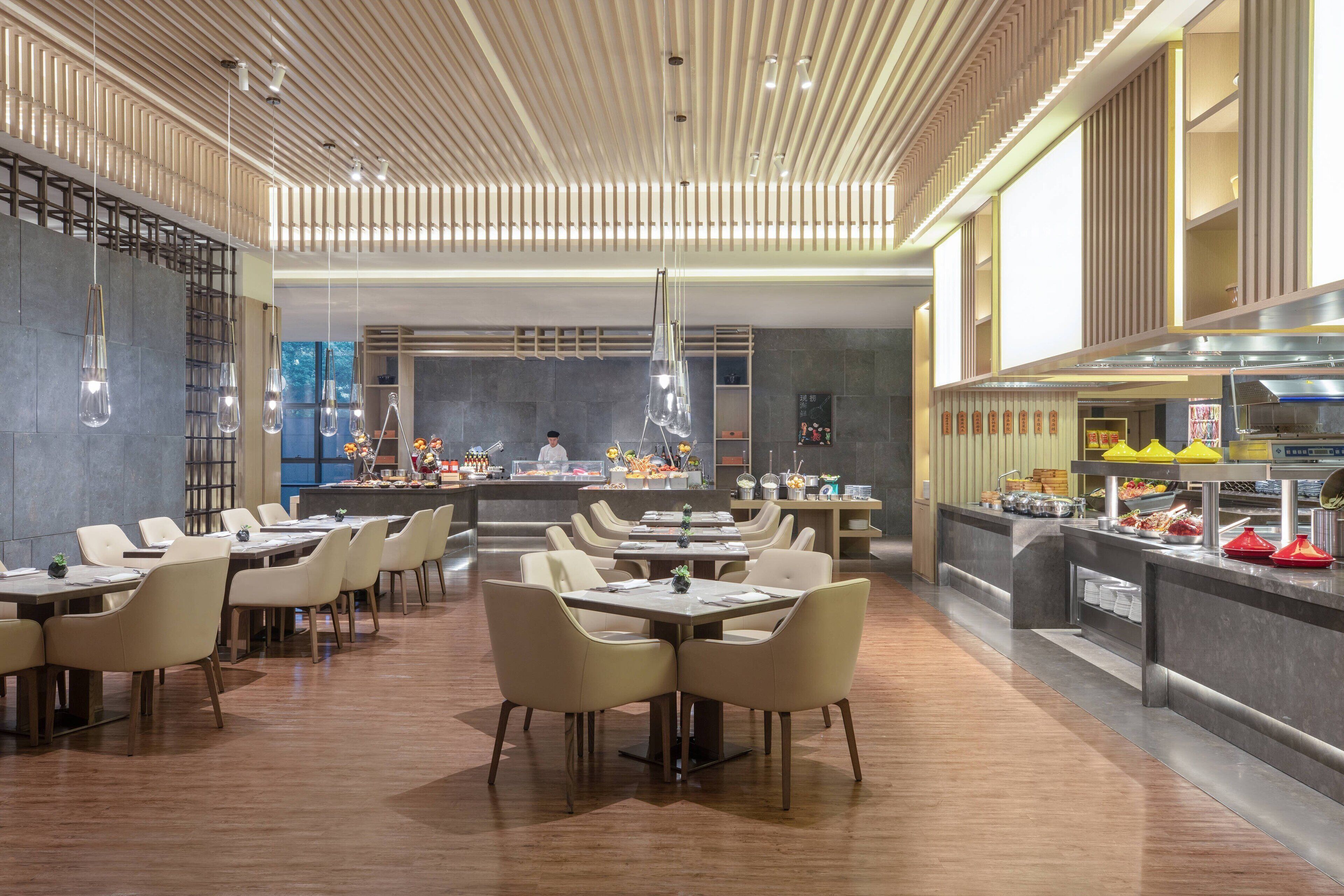 A modern restaurant with multiple dining tables and chairs, a kitchen area, and a bar counter.
