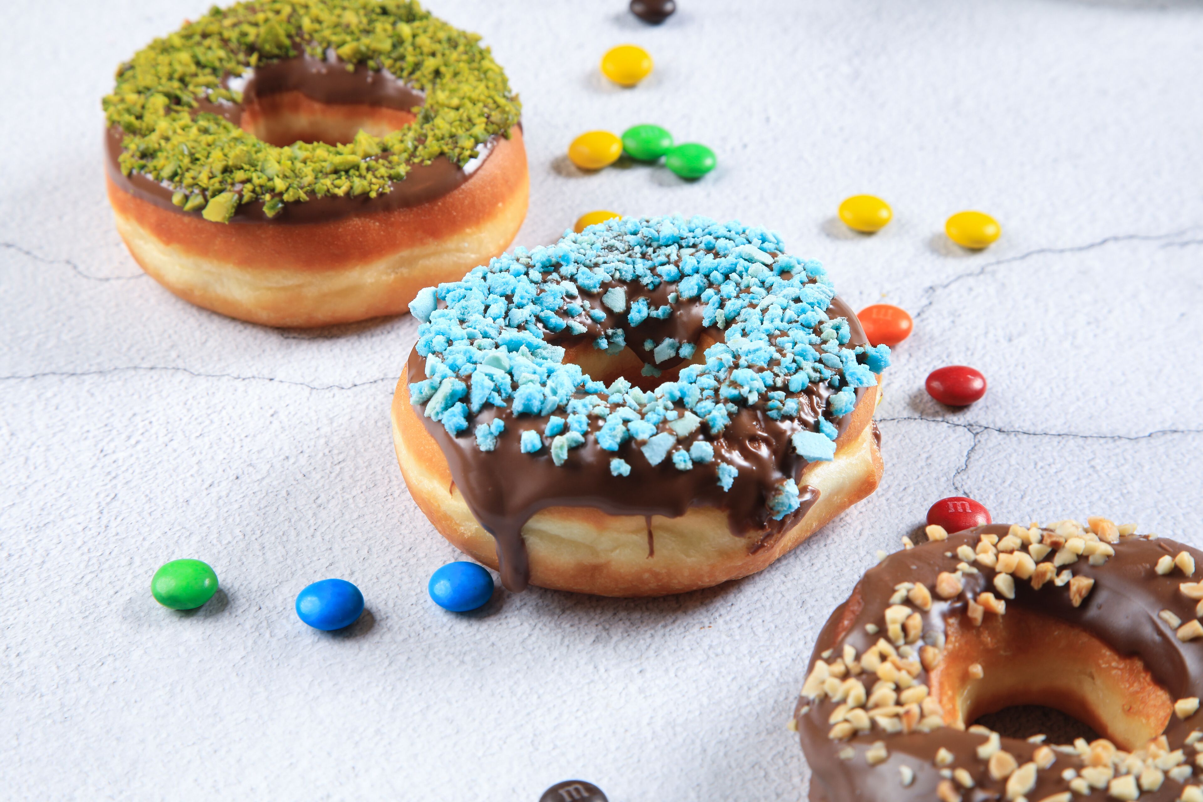 Drie donuts met diverse toppings en kleurrijke snoepjes eromheen.