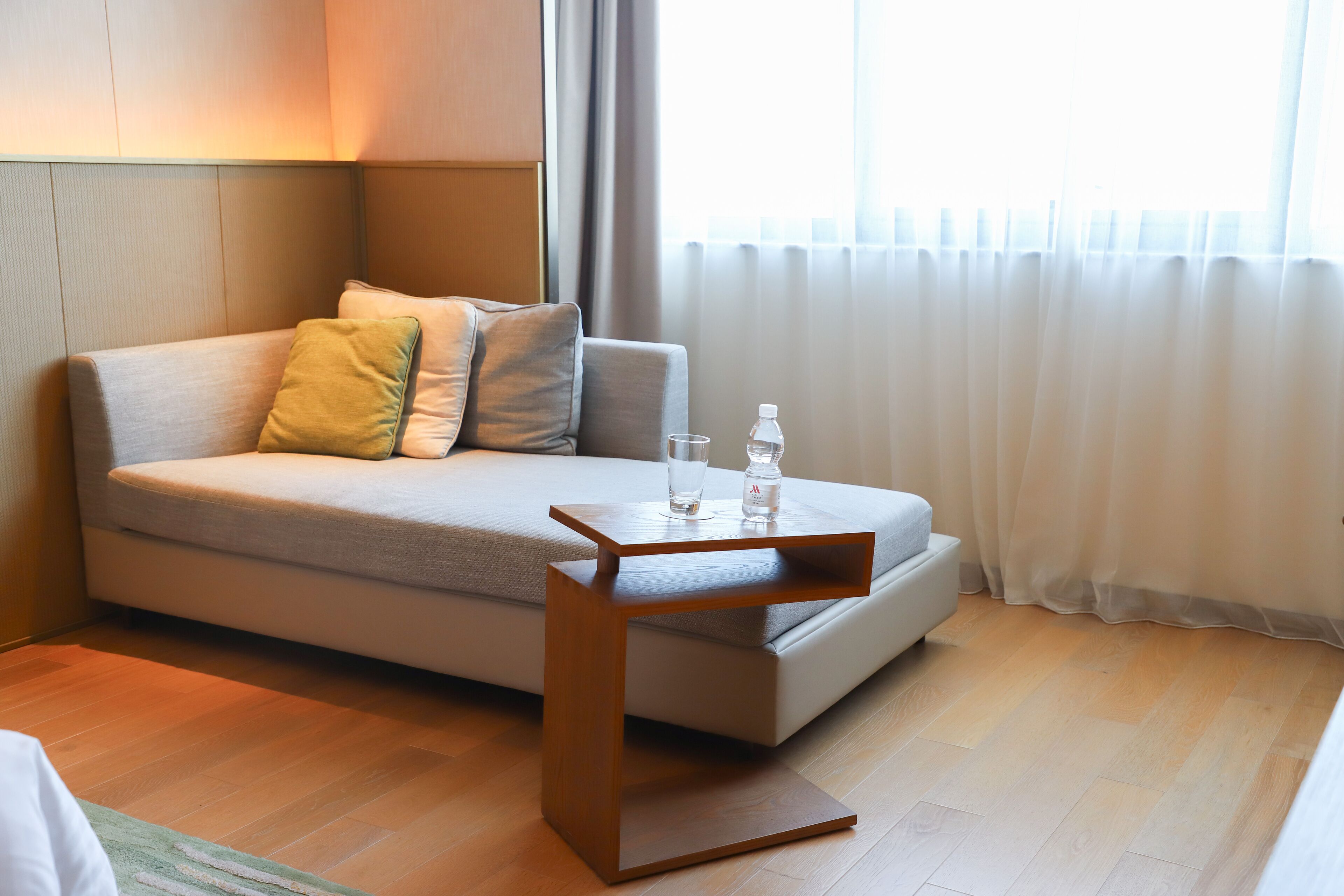 Ein modernes Zimmer mit Schlafsofa, einem Holznachttisch, einem Glas Wasser und einer Flasche auf dem Tisch.