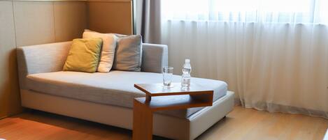 Una habitación moderna con un sofá cama, una mesita de madera, un vaso de agua y una botella sobre la mesa.