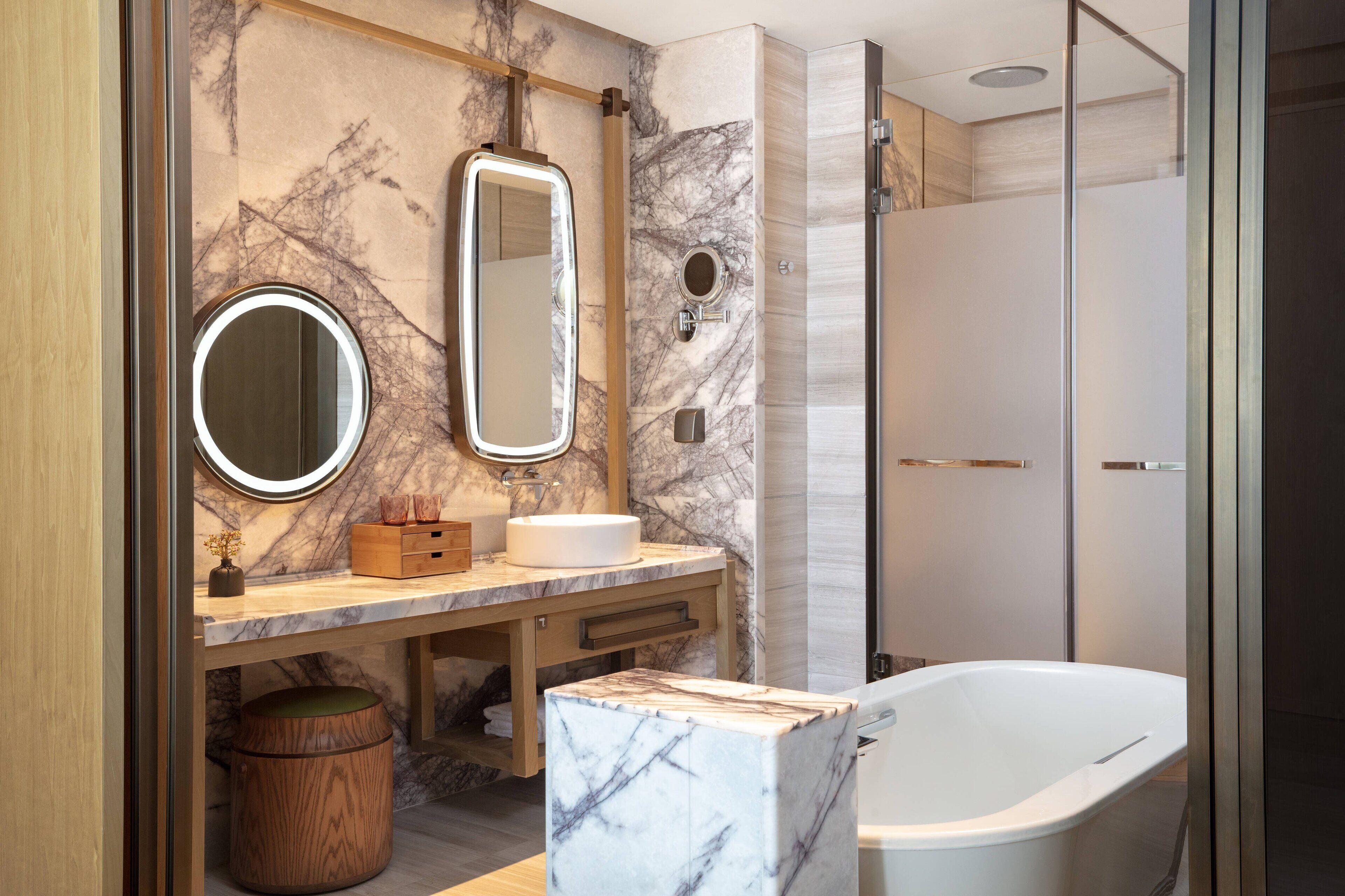 A modern bathroom with a marble vanity, a freestanding bathtub, and a glass-enclosed shower.