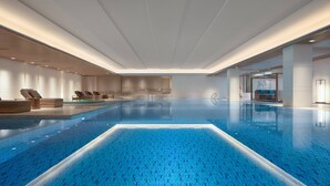 Una piscina interior moderna con suelo de baldosas azules y una zona de solárium con sillones de madera.