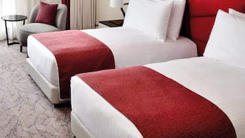 Habitación de hotel con dos camas, una pared de acento roja, una mesa redonda pequeña y una silla.