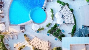 Une piscine sur le toit, de forme circulaire, entourée de chaises longues et de parasols, et un escalier menant à un niveau supérieur.