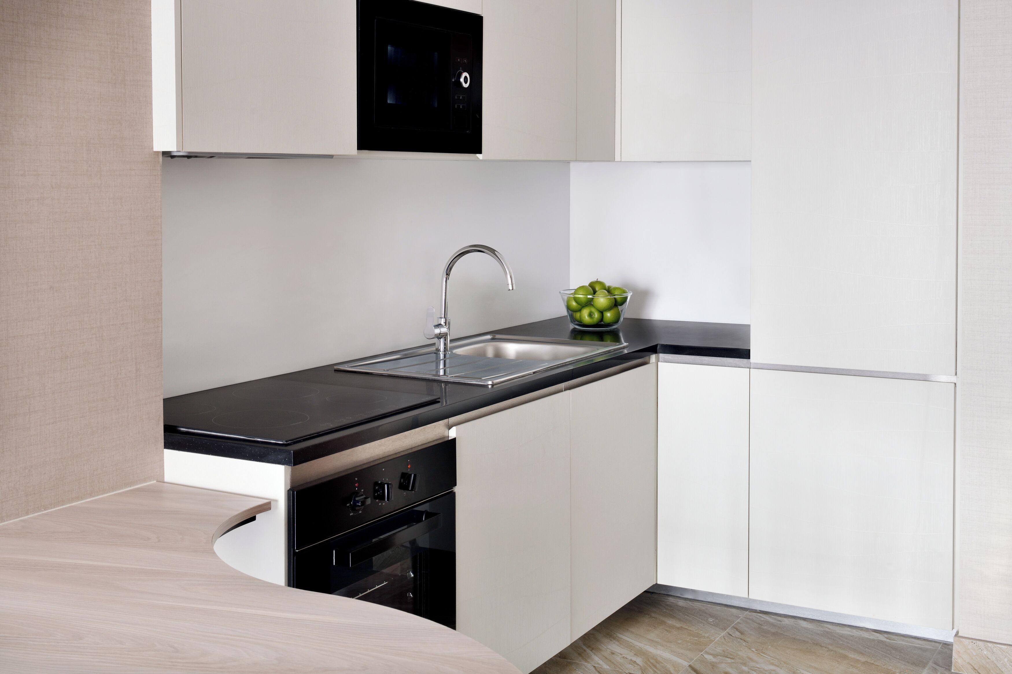A modern kitchen with a black countertop, white cabinets, and a stainless steel sink.