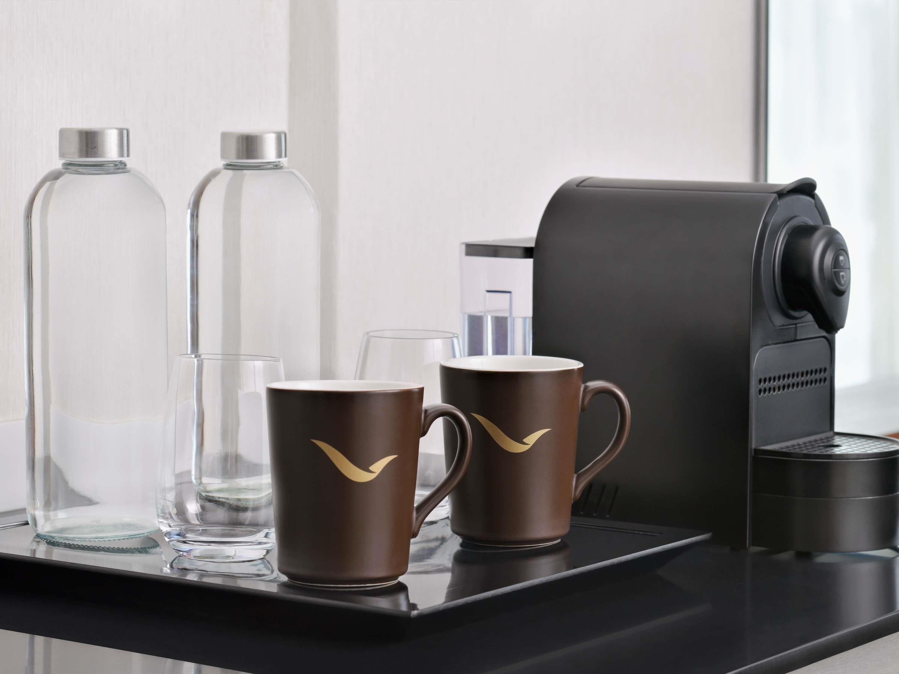 A coffee machine, two coffee cups, and two glass bottles on a tray.