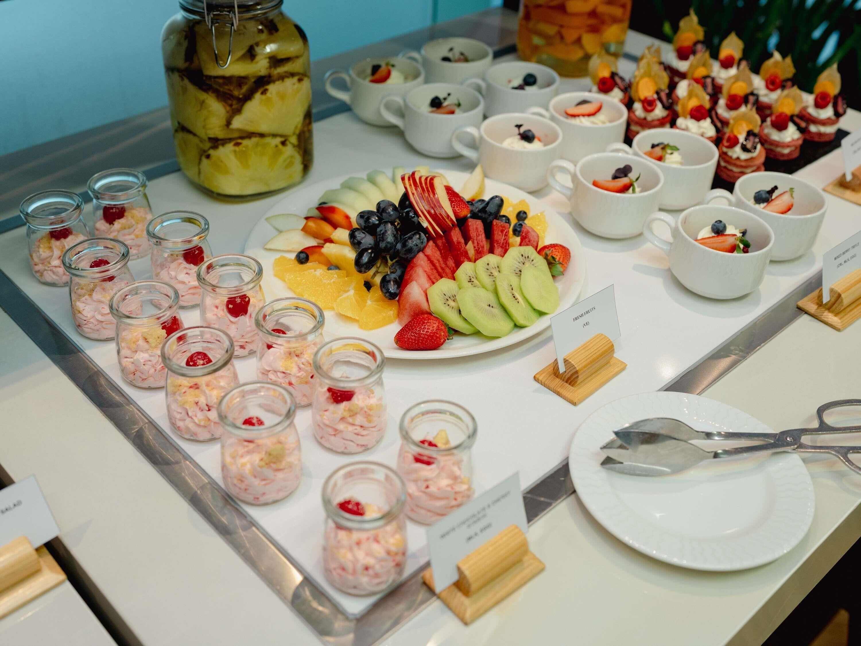 Un buffet proposant une variété de plats, notamment des fruits frais, des desserts et un bocal de cornichons.