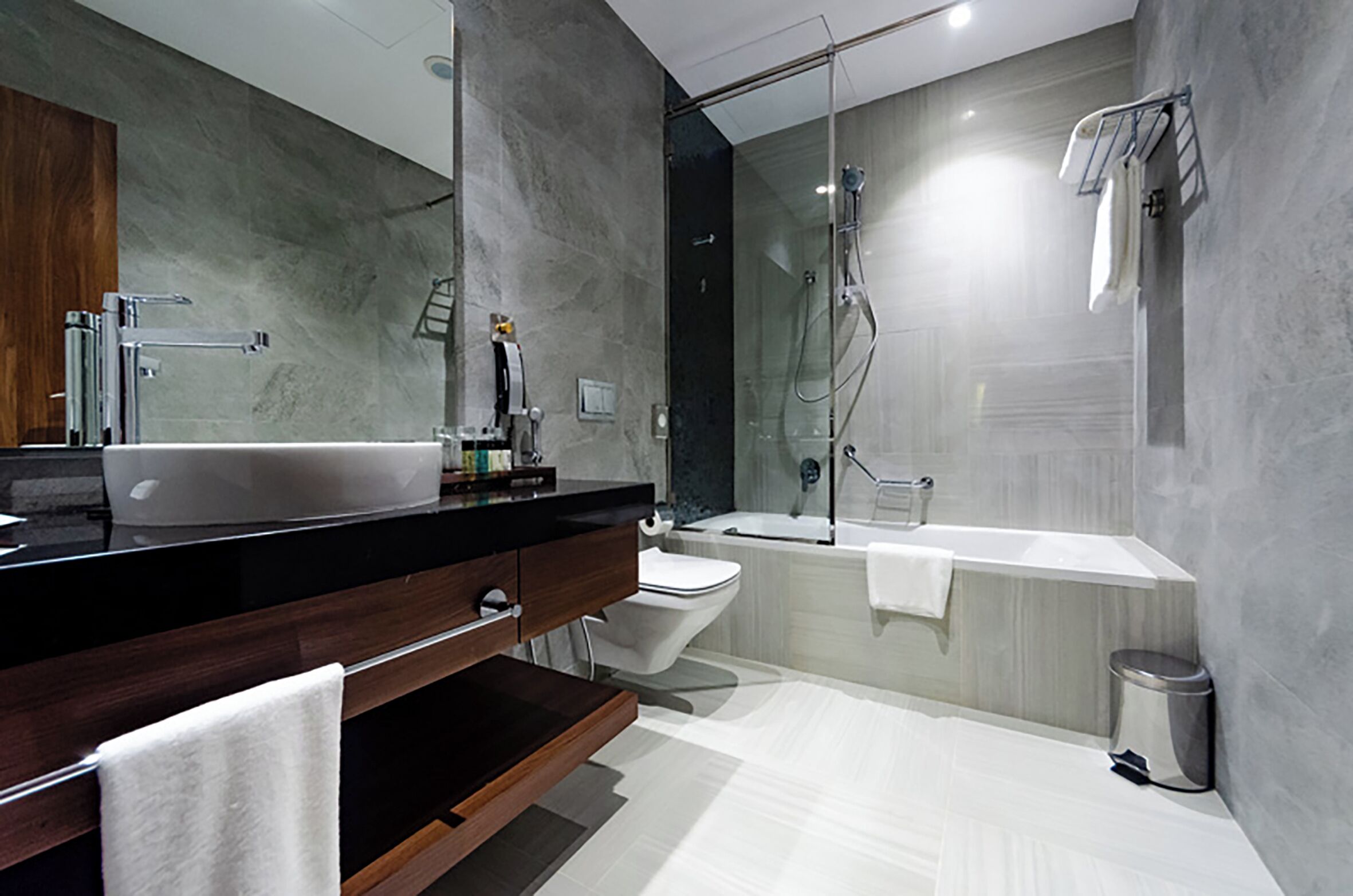 A modern bathroom with a large mirror, a vessel sink, a toilet, a bathtub, and a shower.