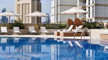 A swimming pool with lounge chairs and umbrellas, surrounded by high-rise buildings.