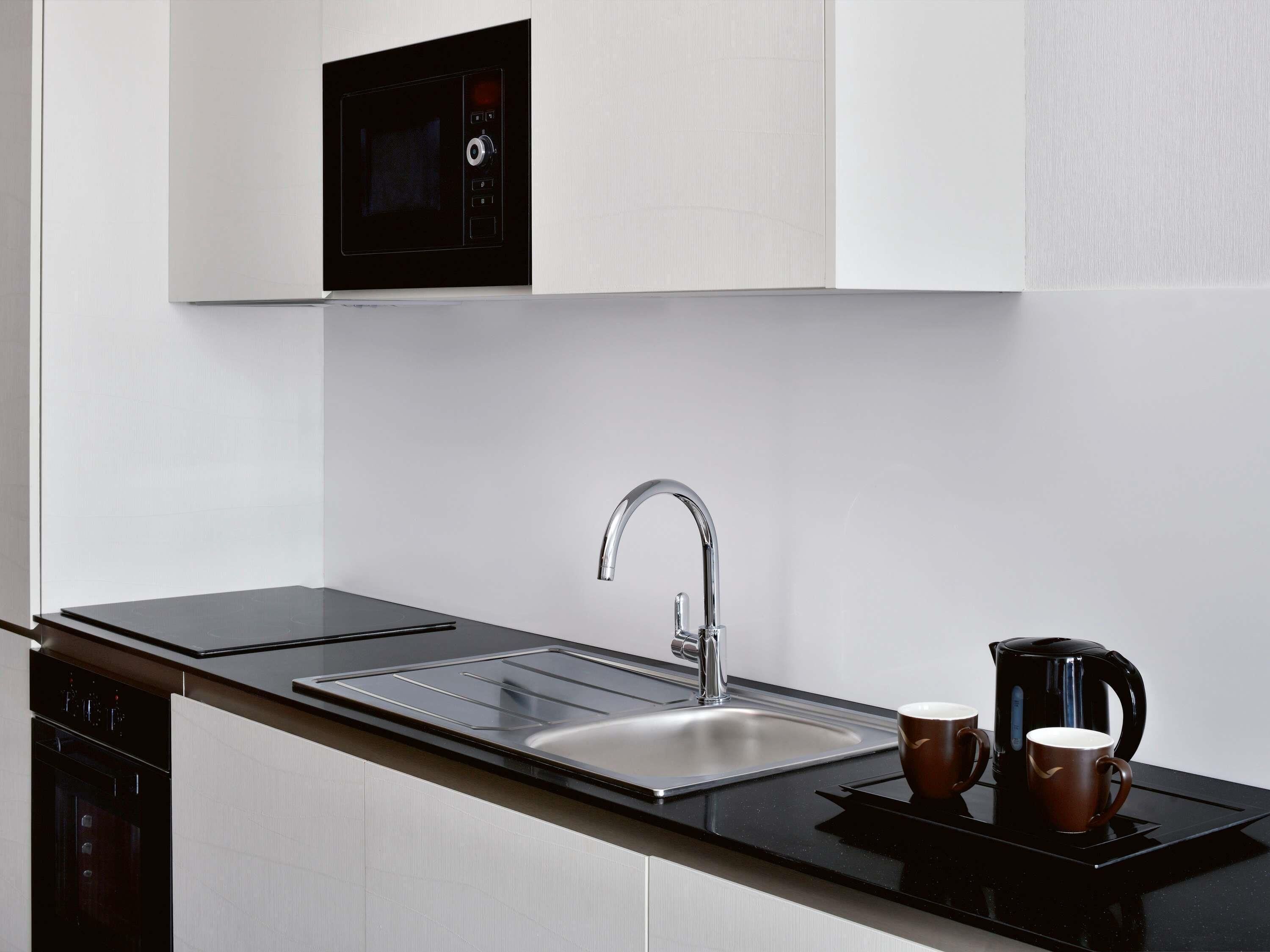 A modern kitchen with a built-in microwave, stainless steel sink, and a kettle on the countertop.