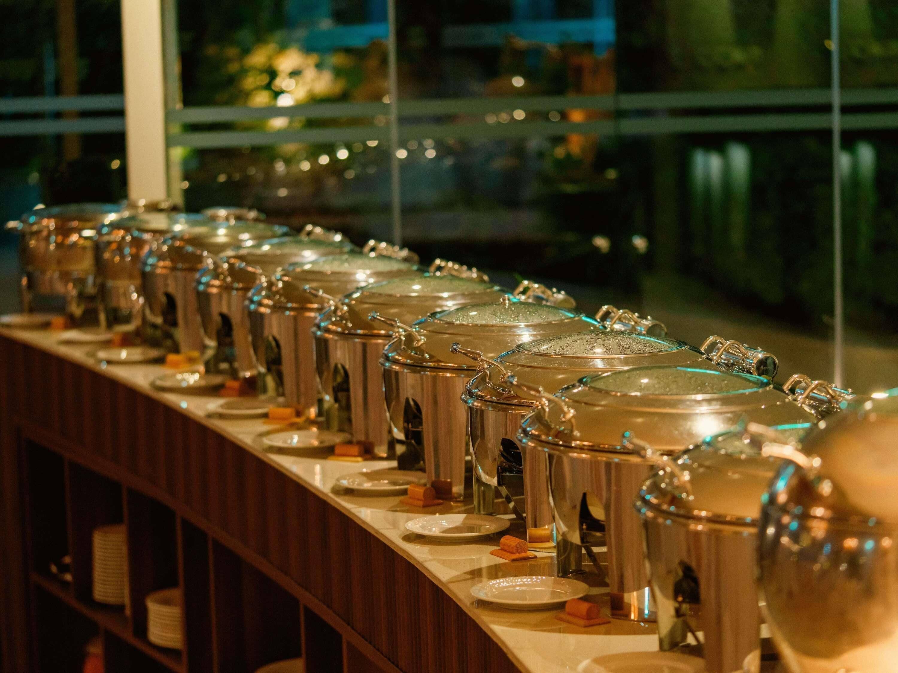 A row of stainless steel beverage dispensers with lids, arranged on a counter.