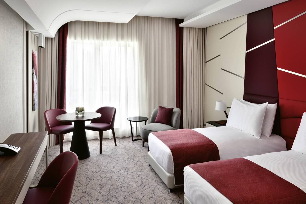 A hotel room with a bed, two chairs, a small table, and a desk.
