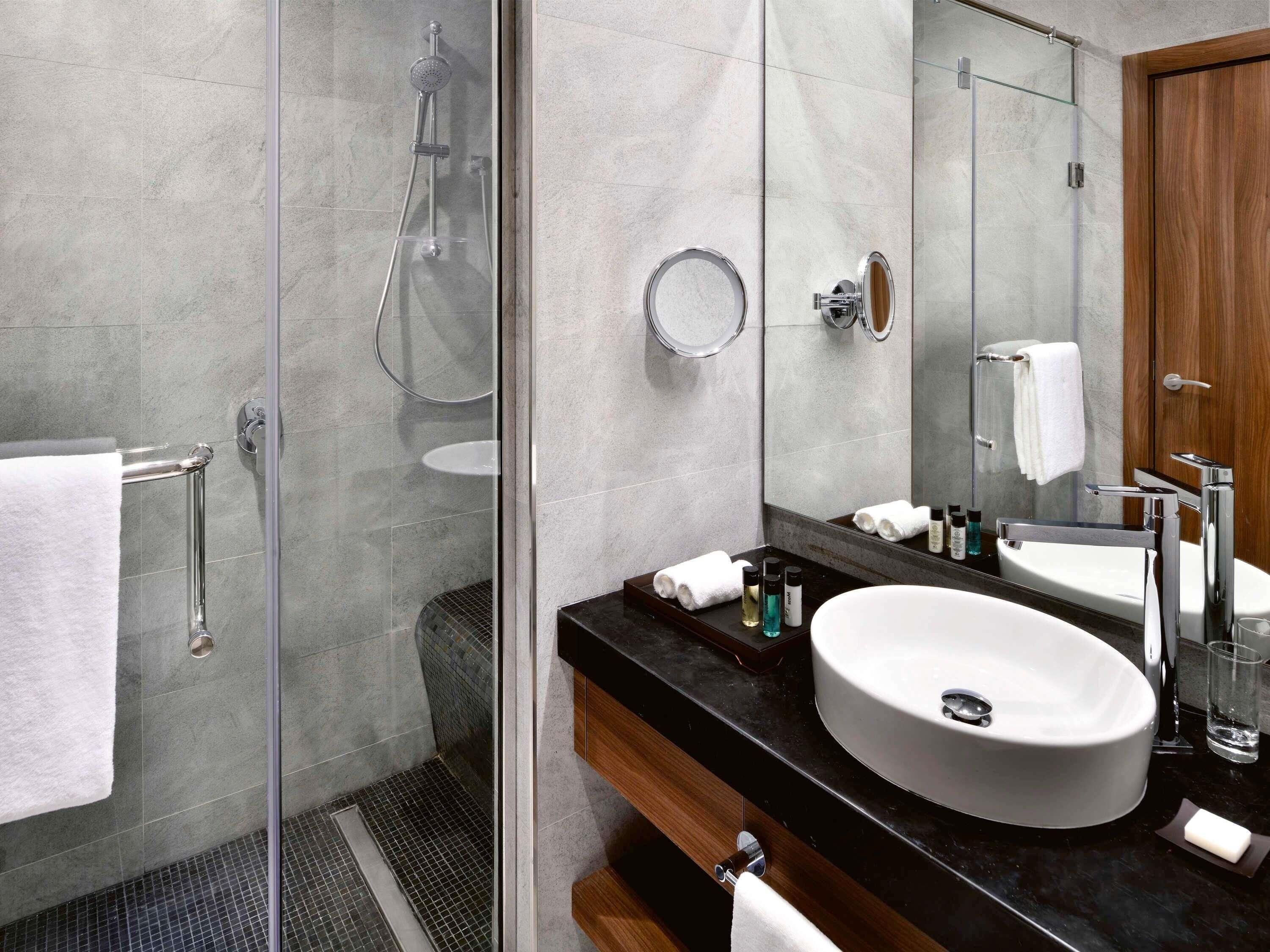 A modern bathroom with a glass-enclosed shower, a large mirror, and a vanity with a sink and countertop.