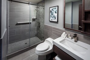 Un baño moderno con ducha envuelta en cristal, inodoro blanco y lavamanos grande.