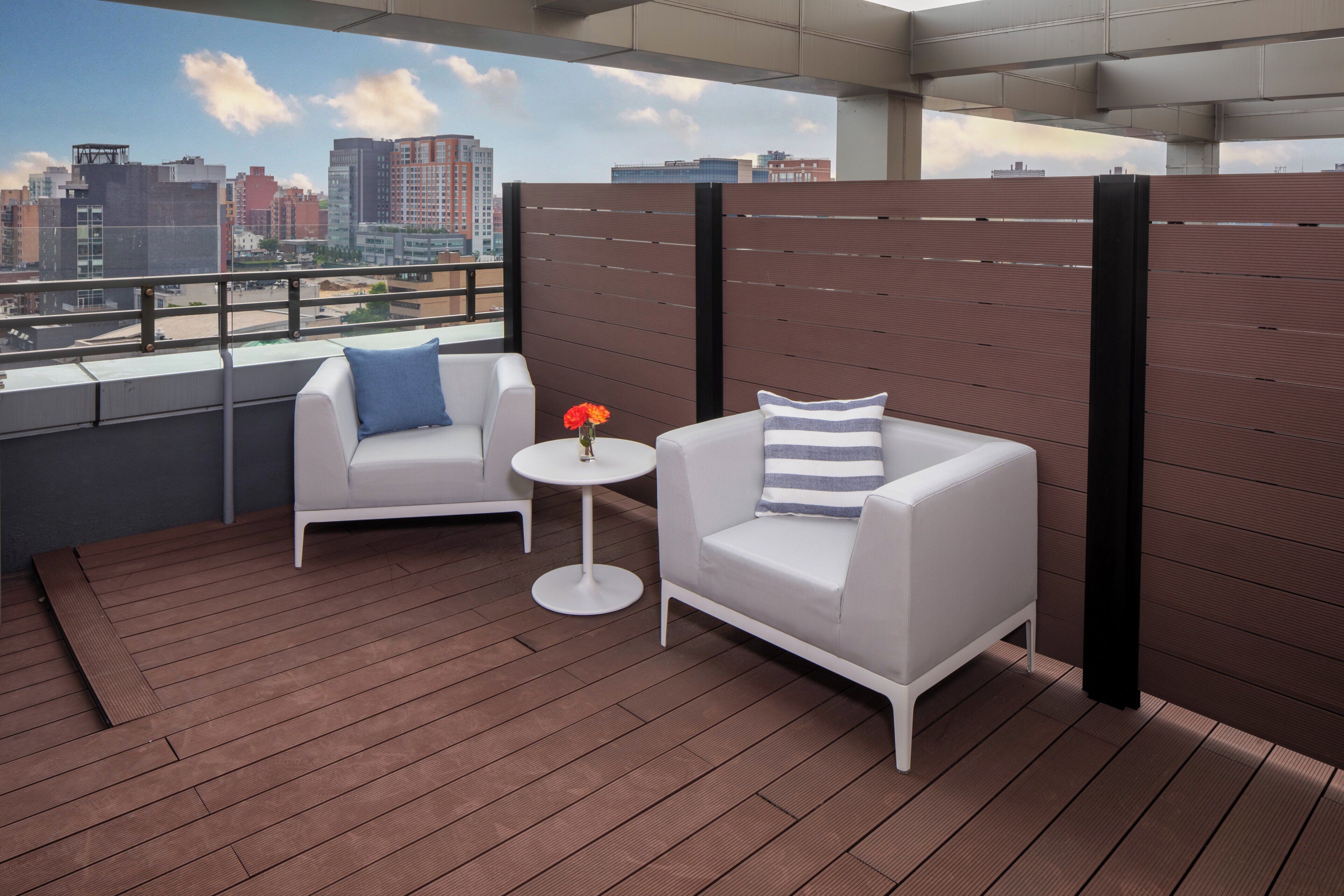 A balcony with two white armchairs, a small round table, and a vase with flowers.