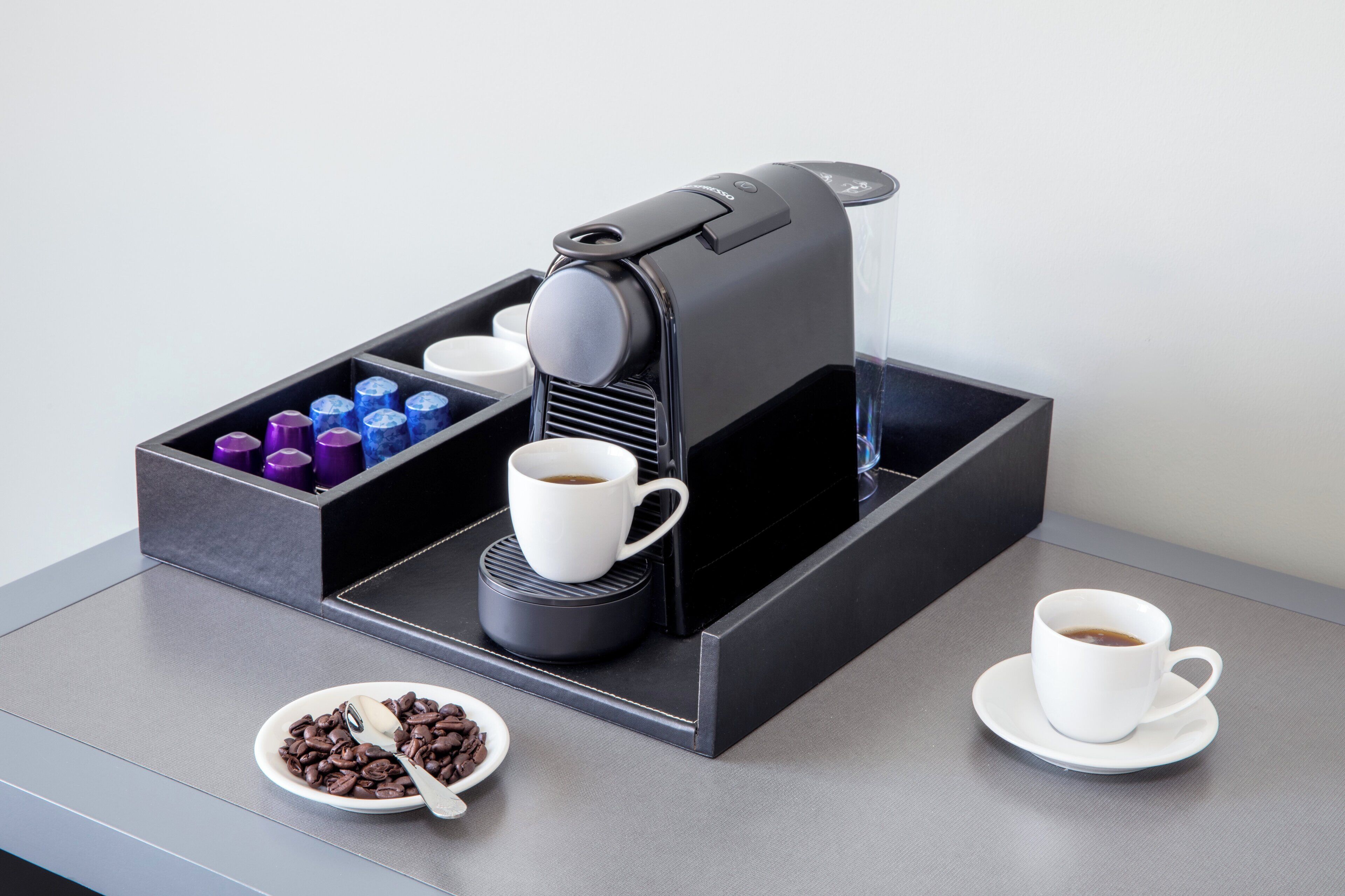 Una cafetera con una bandeja, tazas y un tazón de granos de café.
