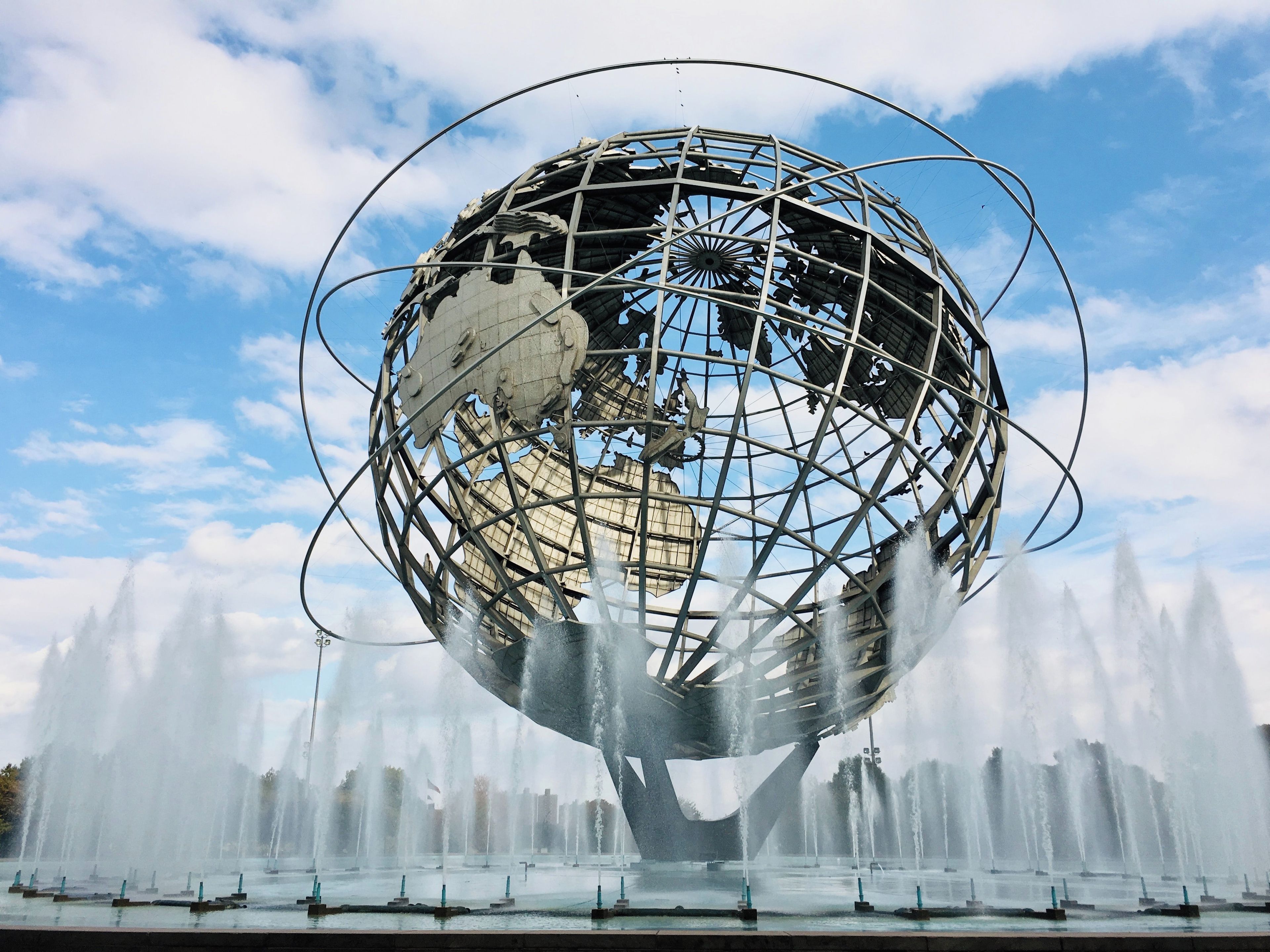 A large metallic globe structure surrounded by a water fountain display.