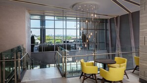 A modern interior with a glass railing, yellow chairs, and a view of the city. - Hotel Indigo Flushing - LaGuardia by IHG (Flushing)
