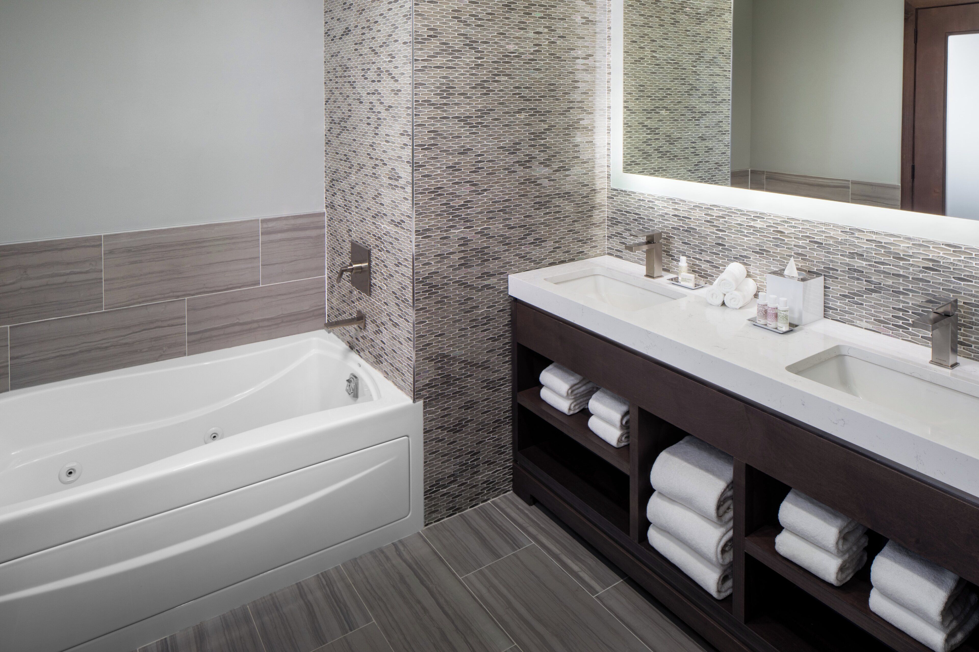 Un baño moderno con bañera, tocador doble y un espejo grande.