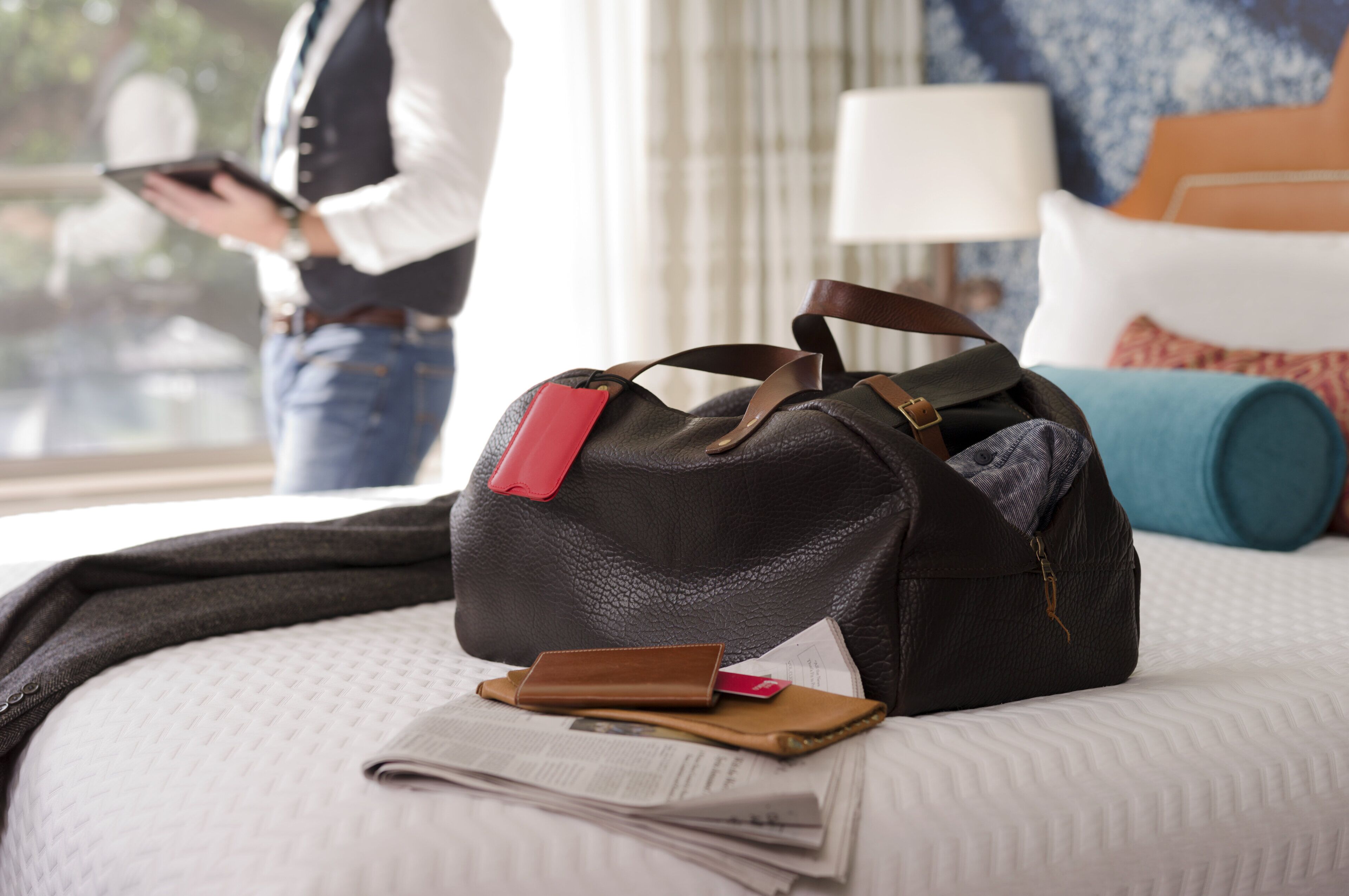 A bed with a black bag, a brown wallet, and a red card on it.