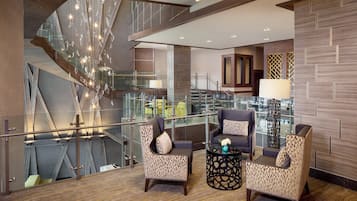 Experience the hotel's contemporary design, featuring a high ceiling, geometric light fixture, and a spacious seating area with patterned armchairs and a round coffee table.