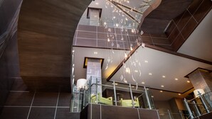 A modern interior with a curved staircase, glass railings, and a chandelier. - Hotel Indigo Flushing - LaGuardia by IHG (Flushing)
