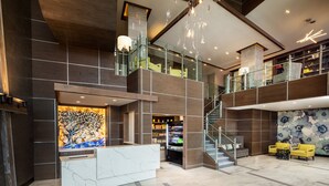 A modern lobby with a marble reception desk, a staircase, and a seating area with yellow chairs. - Hotel Indigo Flushing - LaGuardia by IHG (Flushing)