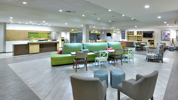 A spacious lobby with a reception desk, green seating area, and multiple tables and chairs. - Home2 Suites by Hilton Duncan (Duncan)