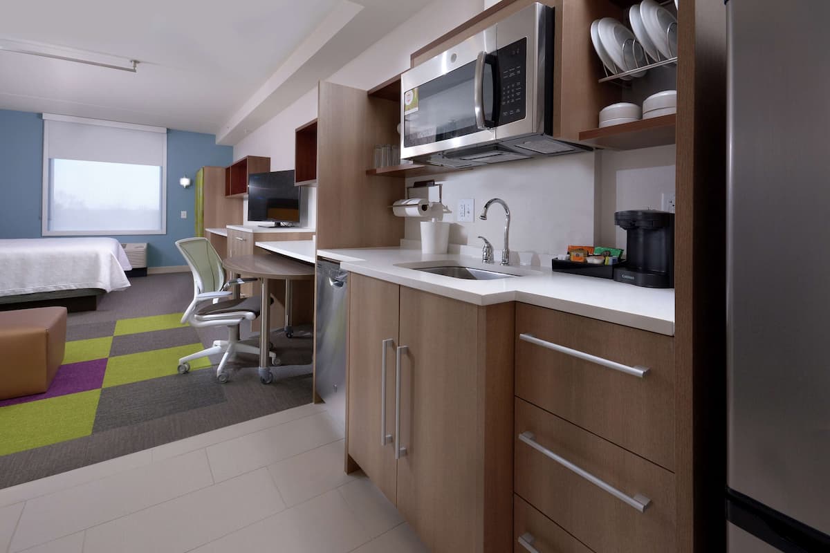 A modern hotel room with a kitchenette, a bed, a desk, and a chair.
