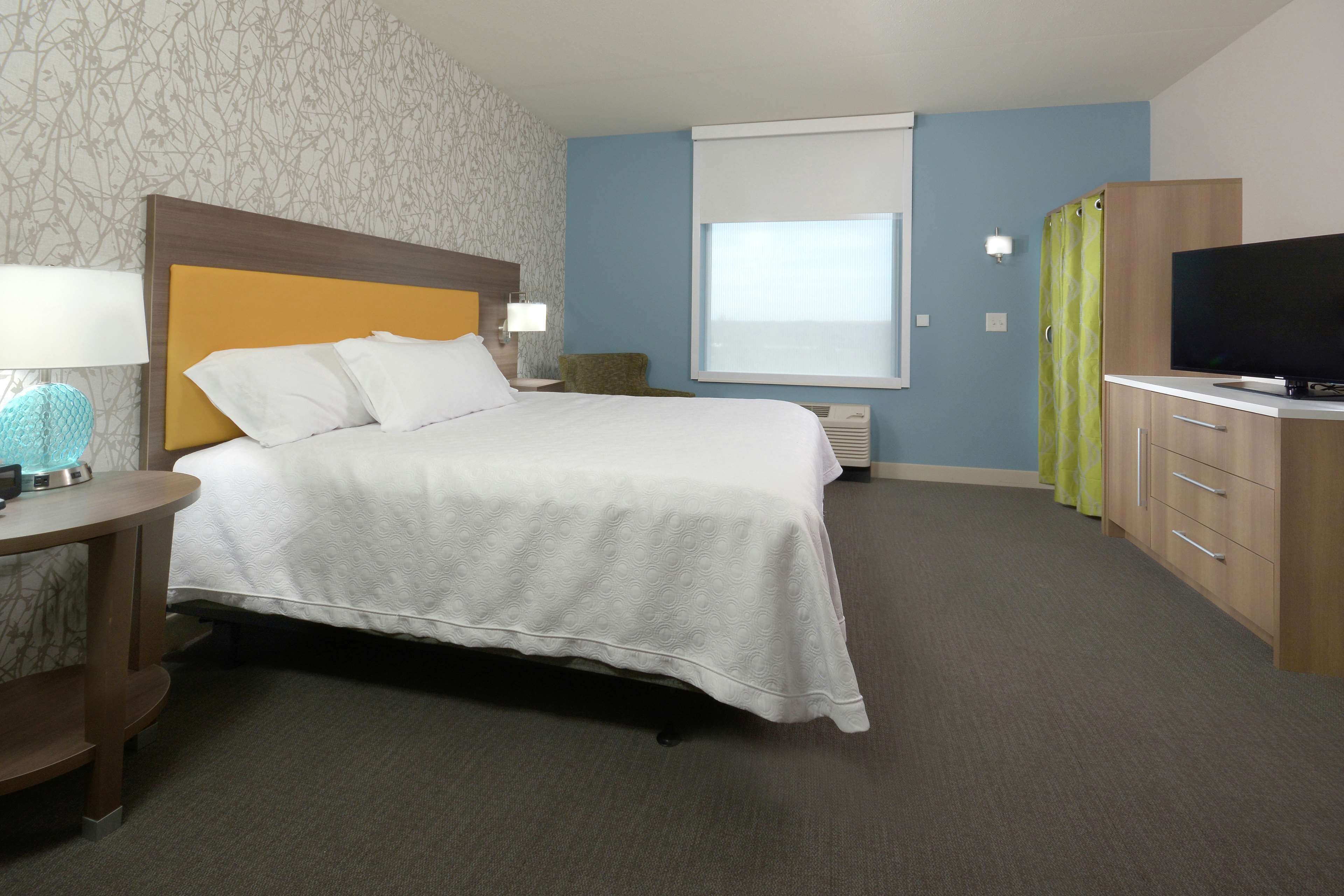 Ein Hotelzimmer mit einem Bett, einem Fernseher, einem Schreibtisch mit Lampe und einem Vorhangfenster.