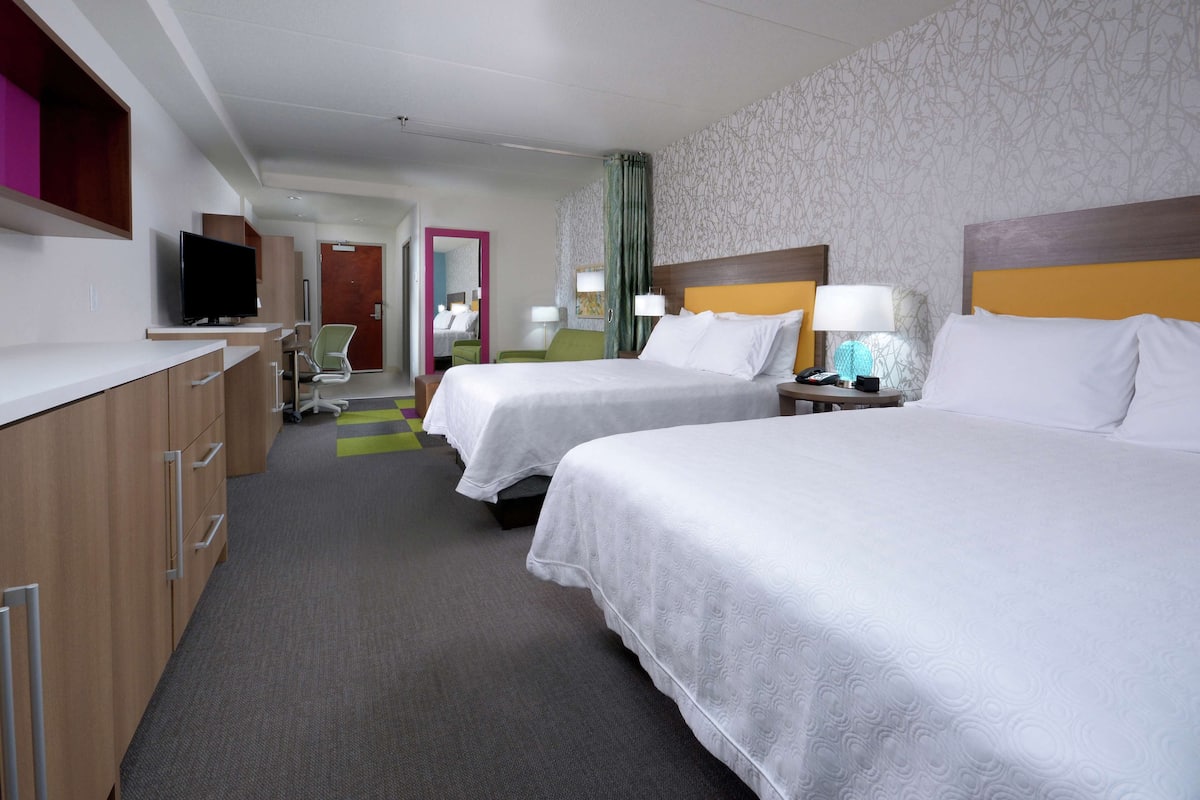 A hotel room with two beds, a TV, a desk, and a chair.