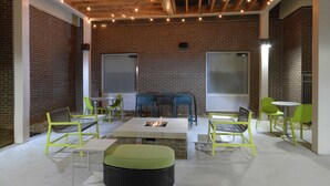 An outdoor patio area with brick walls, a fire pit, and several chairs and tables. - Home2 Suites by Hilton Duncan (Duncan)