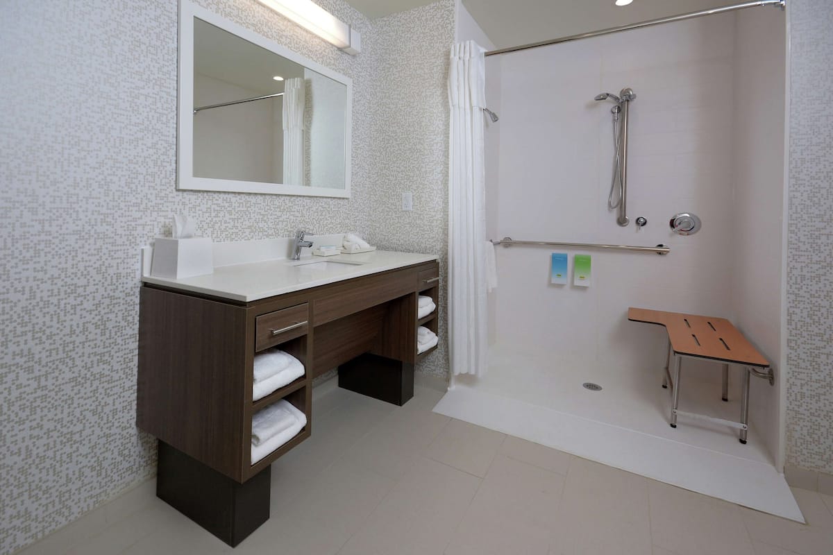 A bathroom with a shower, a sink with a mirror, and a bench.